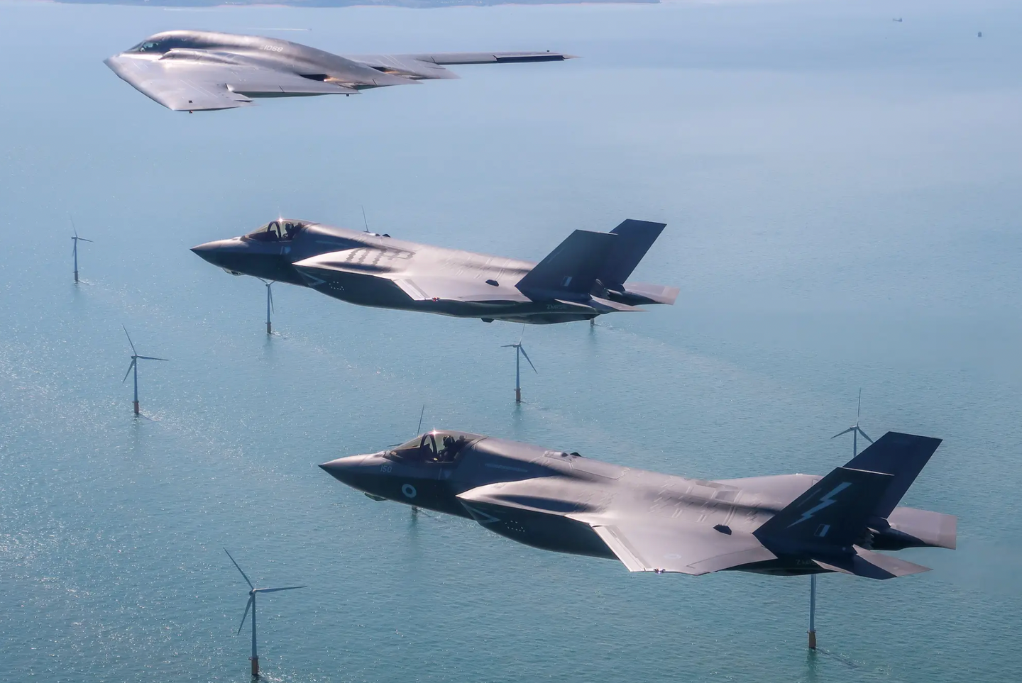 Two Royal Air Force F-35Bs (with ZM152 further from the camera) accompany a U.S. Air Force B-2 stealth bomber over the English coast during integration flying training in 2019. <em>Crown Copyright</em>