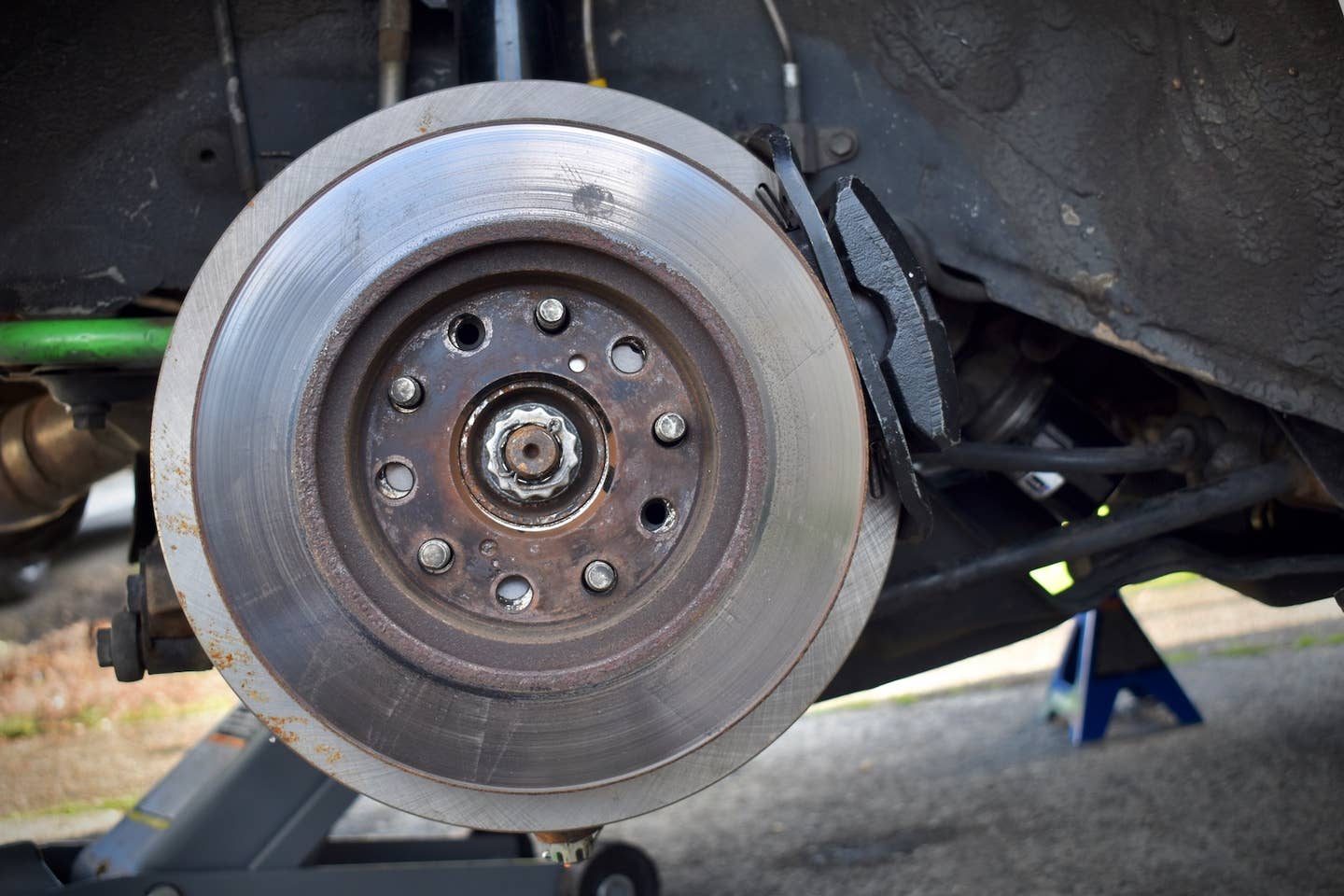 A small brake rotor sits on the lugs with a new, larger rotor and caliper behind it