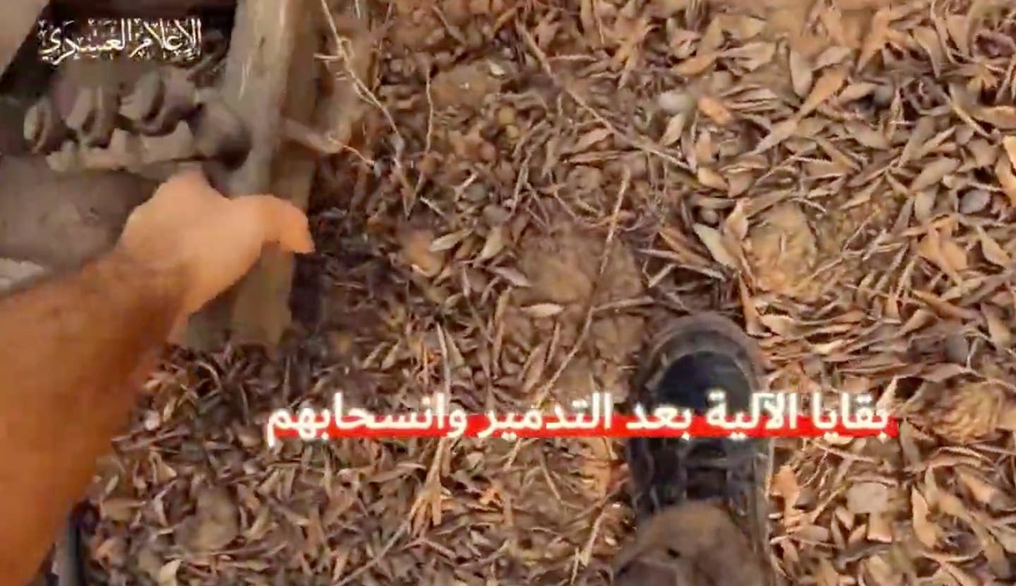 A Hamas fighter picks up a piece of metal, presumably after the attack on the tank.