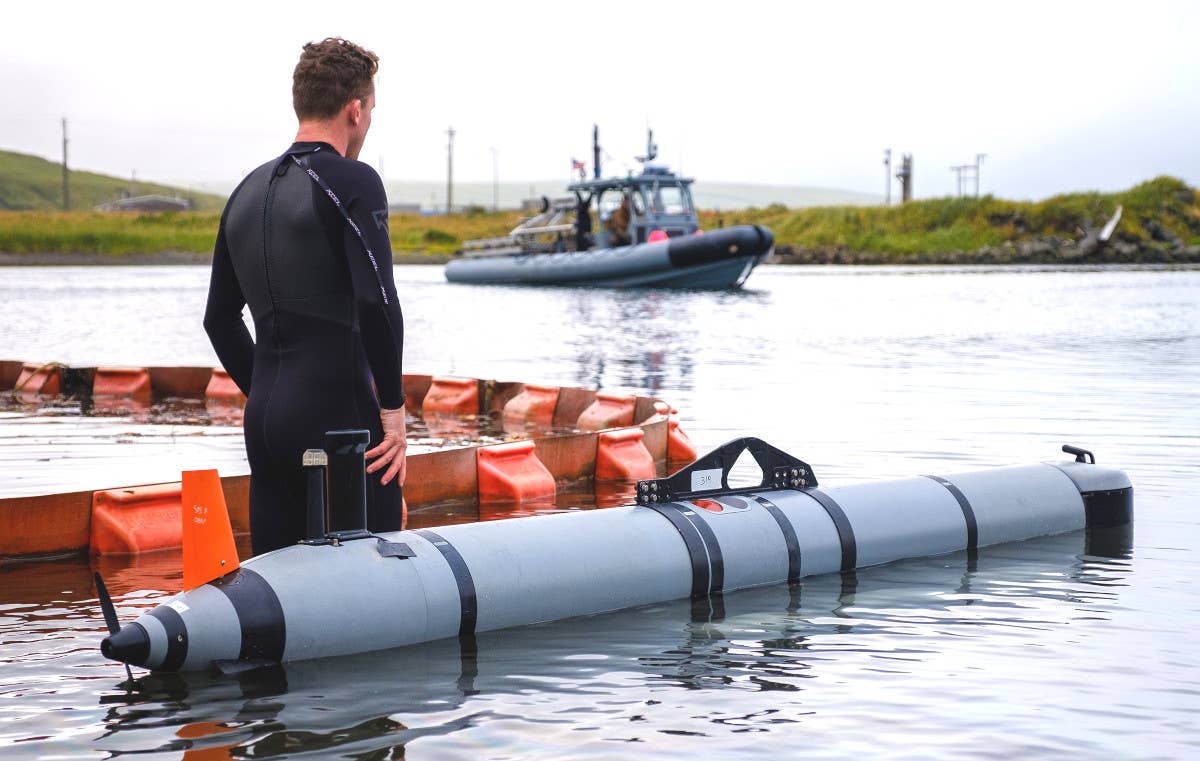 A US Navy Mk 18 Mod 2 Kingfish UUV. Its antenna mast, as well as its emergency locator beacon immediately behind it, both colored in black, are seen sticking up from the top of the rear of the body. In the middle of the body is also a handle used to launch and recover the drone on the surface. <em>USN</em>