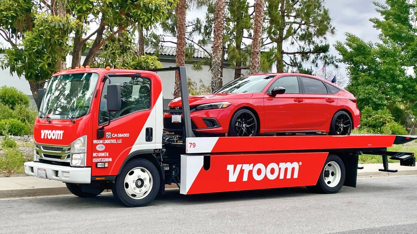 A red Honda Civic on the back of a flatbed track with prominent Vroom branding