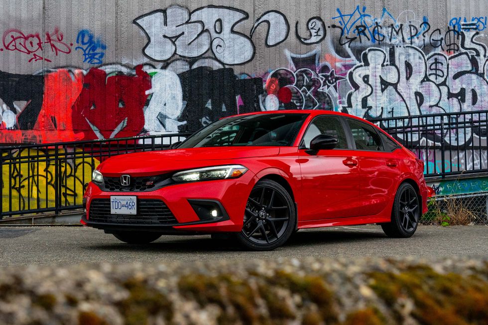 a red car parked in front of a wall with graffiti